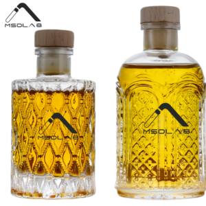 Two 350ml glass liquor bottles with different embossed relief patterns and wooden stoppers, filled with amber liquid.